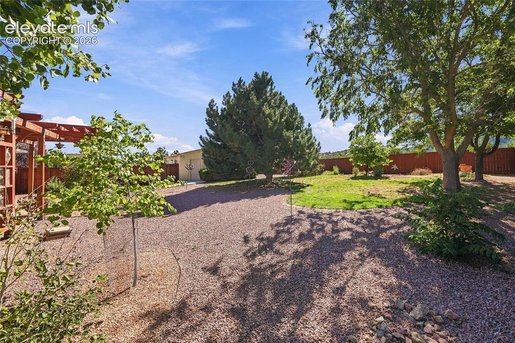 Image 25 of 36: Expansive outdoor space featuring a pergola, gravel pathways, a grass lawn,