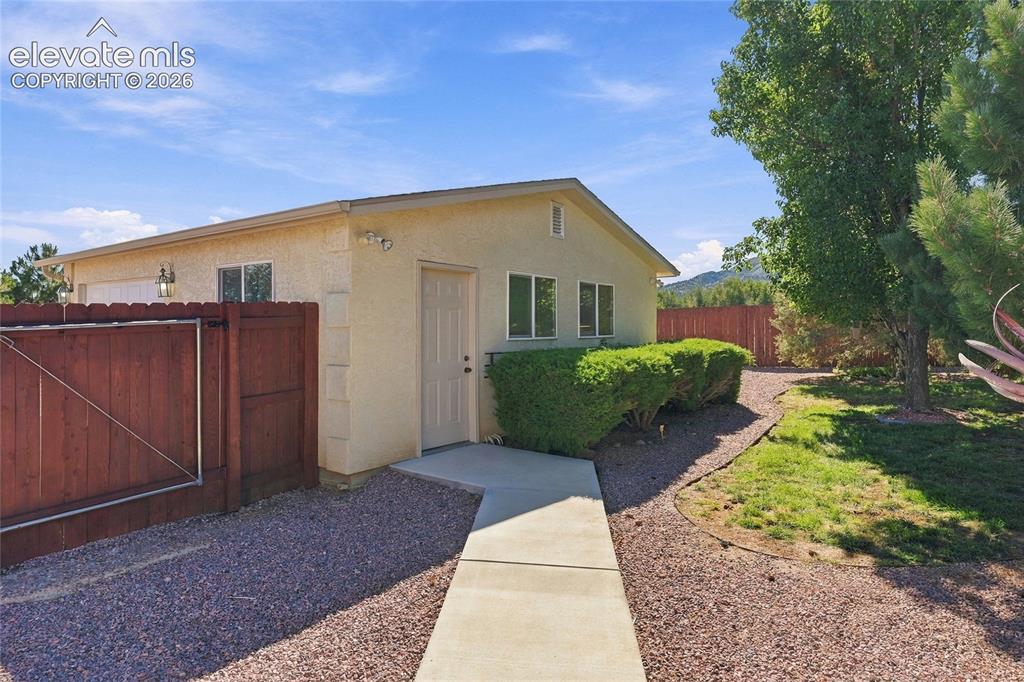 Image 29 of 36: Stucco exterior with a concrete walkway, gravel landscaping, and a wooden p