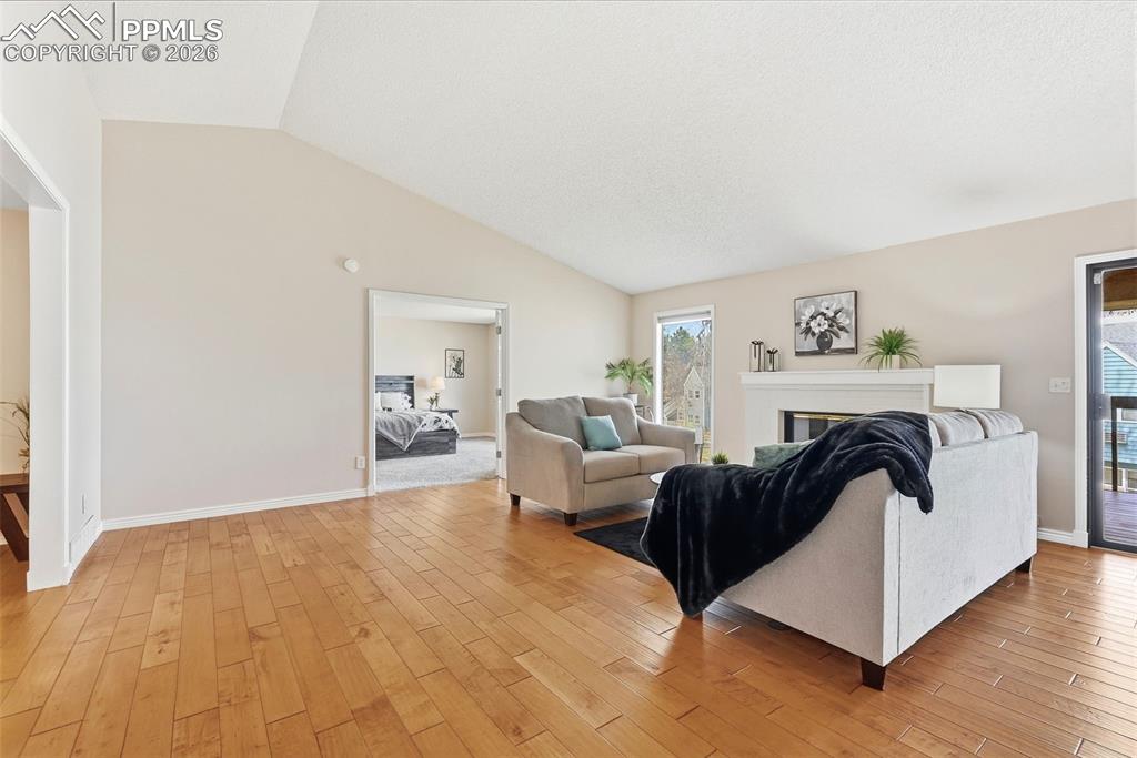 Image 16 of 44: Spacious living area featuring hardwood floors, vaulted ceilings, a firepla