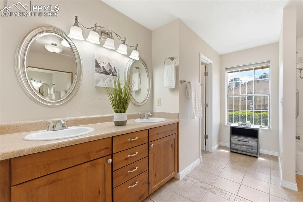Image 19 of 44: The bathroom features a double vanity with light wood cabinetry, two oval m