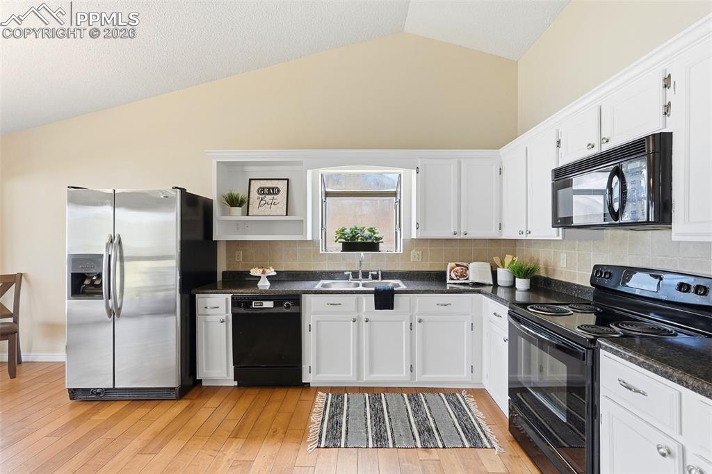 Image 3 of 44: The kitchen features white cabinetry, black countertops, and a tiled backsp