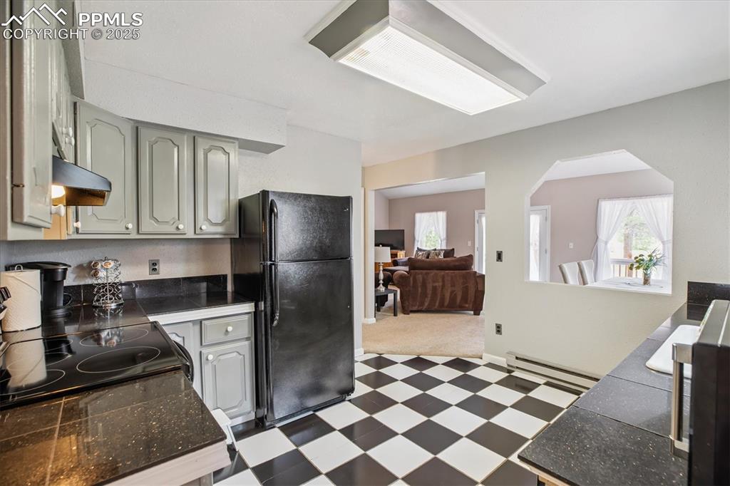 Image 13 of 29: Kitchen with dark floors, freestanding refrigerator, baseboard heating, and