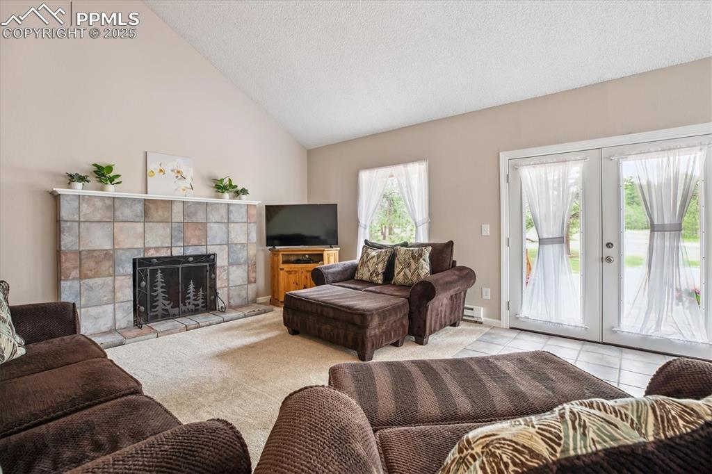 Image 6 of 29: Living room featuring a tiled fireplace, french doors, vaulted ceiling and
