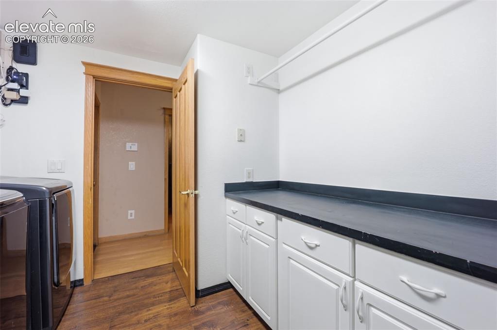 Image 14 of 49: Built-in white cabinetry, dark countertop, wood-finish flooring, and natura