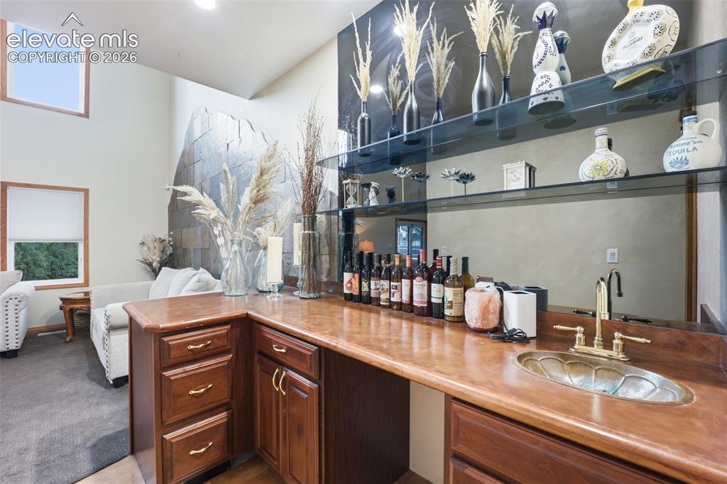 Image 20 of 49: Built-in wet bar with wood cabinetry, a decorative basin sink, and brass fi
