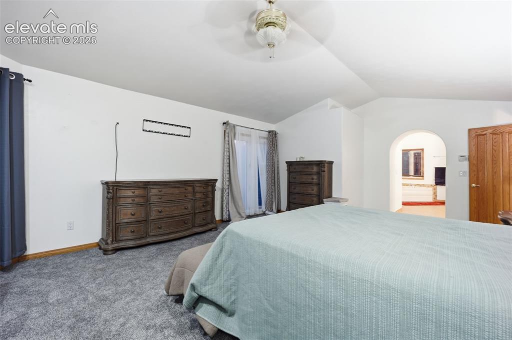 Image 28 of 49: Carpeted flooring, vaulted ceiling, arched doorway, and a wood-panel door