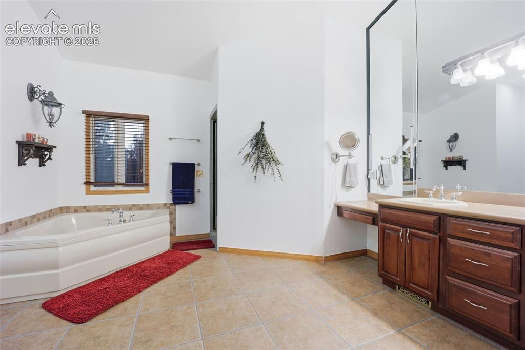 Image 29 of 49: Tile flooring, built-in soaking tub with tile surround, wood-finish vanity
