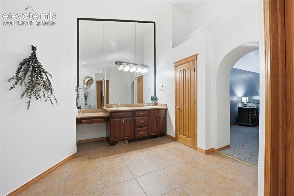 Image 30 of 49: Double vanity with integrated makeup counter, multiple mirrors, and tile fl
