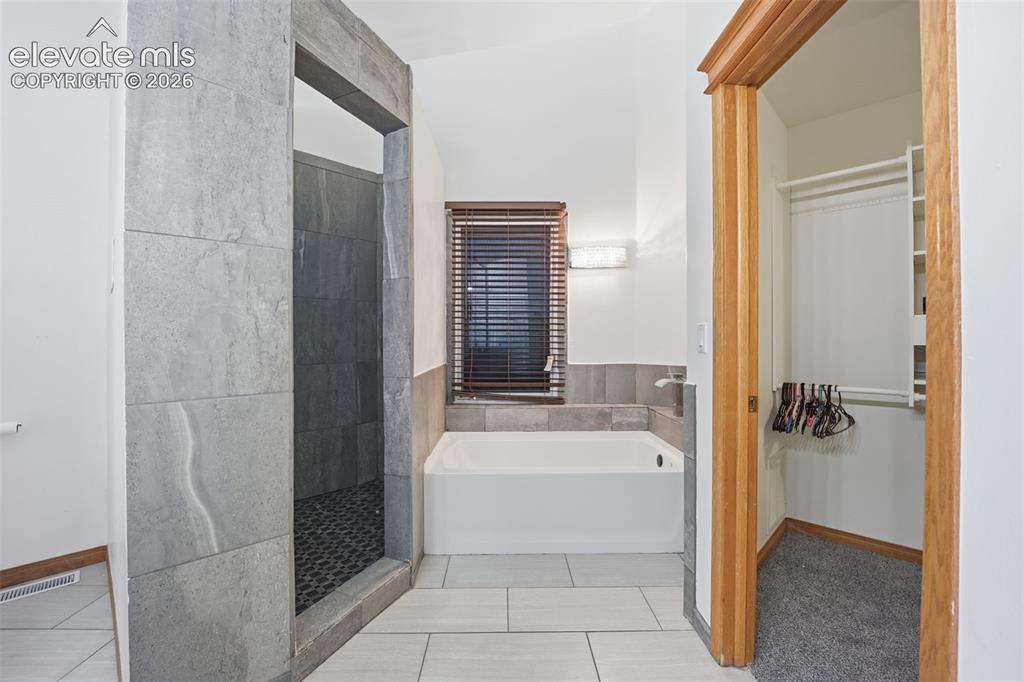 Image 35 of 49: Tiled shower enclosure, soaking tub, window with blinds, and built-in close