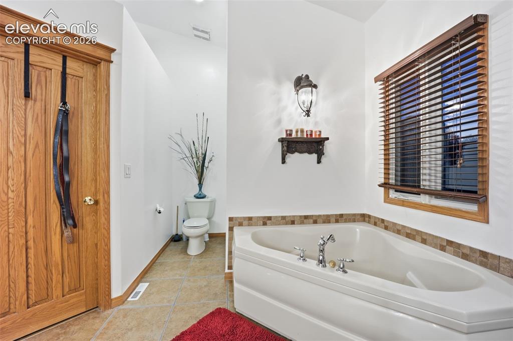 Image 36 of 49: Corner soaking tub with polished chrome fixtures, tile surround, wood-slat