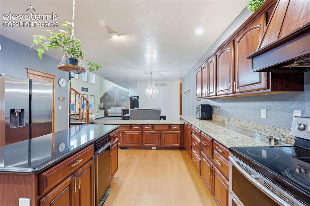 Image 4 of 49: Kitchen featuring wood cabinetry, granite countertops, an island with a dar