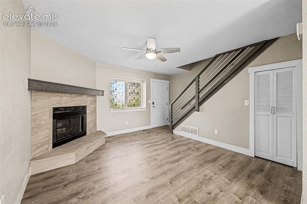 Image 7 of 31: Tiled fireplace with a wood mantel, wood-finish flooring, modern metal stai