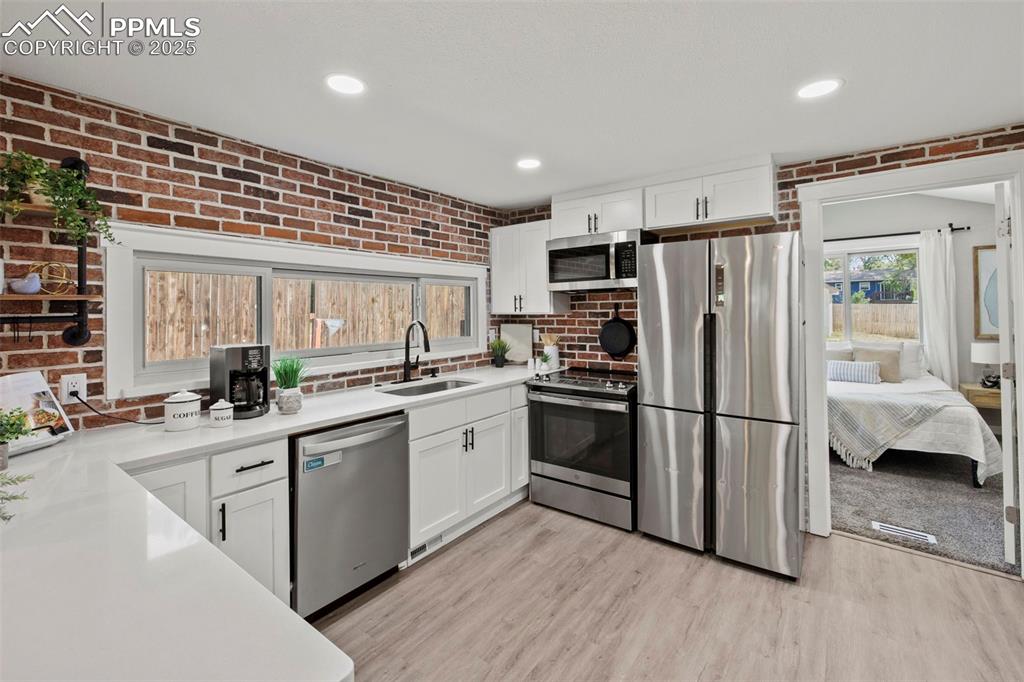Image 3 of 27: Kitchen featuring stainless steel appliances, brick wall, white cabinetry,