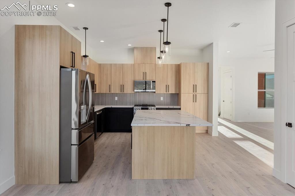Image 11 of 30: Kitchen with pendant lighting, a center island, light stone counters, and s