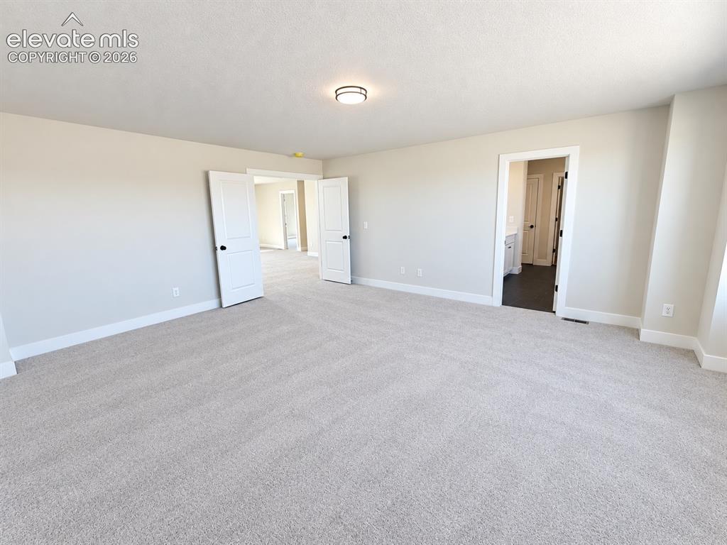 Image 15 of 26: Spacious room with light neutral wall tones, plush carpeting, and recessed