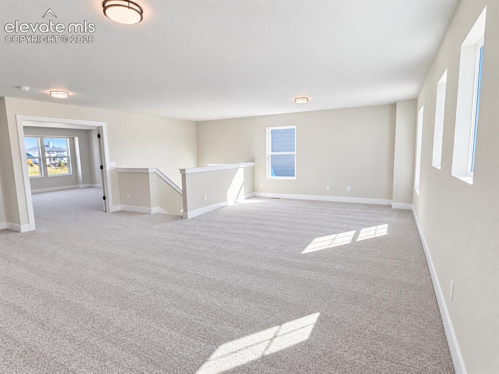 Image 8 of 26: Expansive carpeted space featuring multiple windows, a staircase with a hal