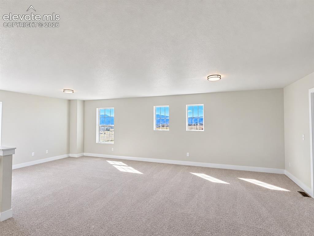 Image 9 of 26: Expansive room featuring light-colored carpeting, multiple windows, and two
