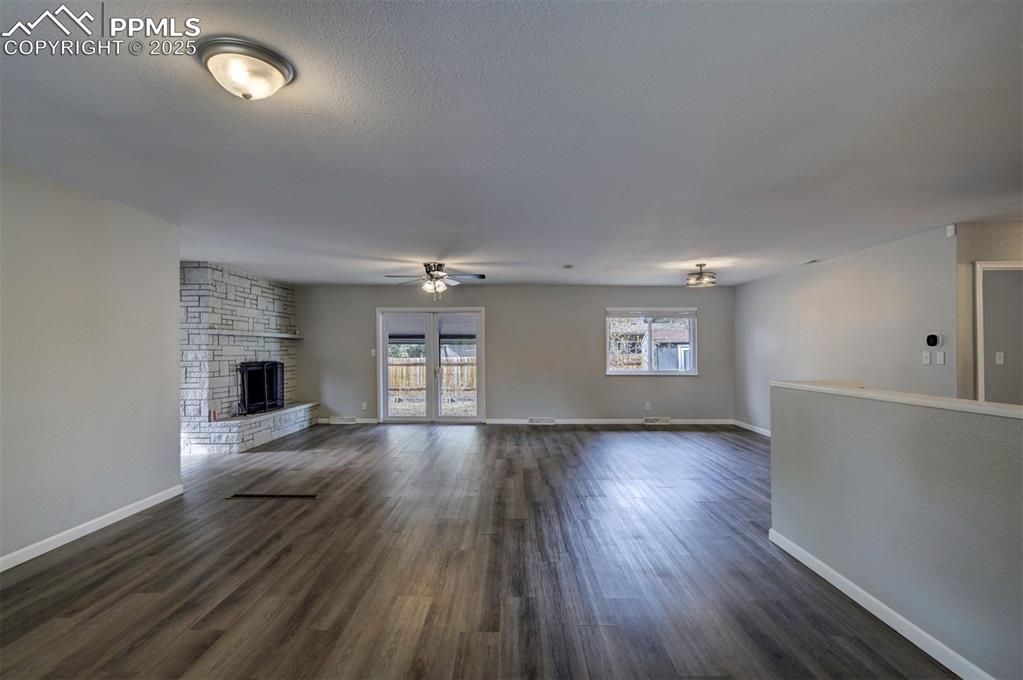 Image 12 of 43: Unfurnished living room with wood-style flooring, a stone fireplace, and a