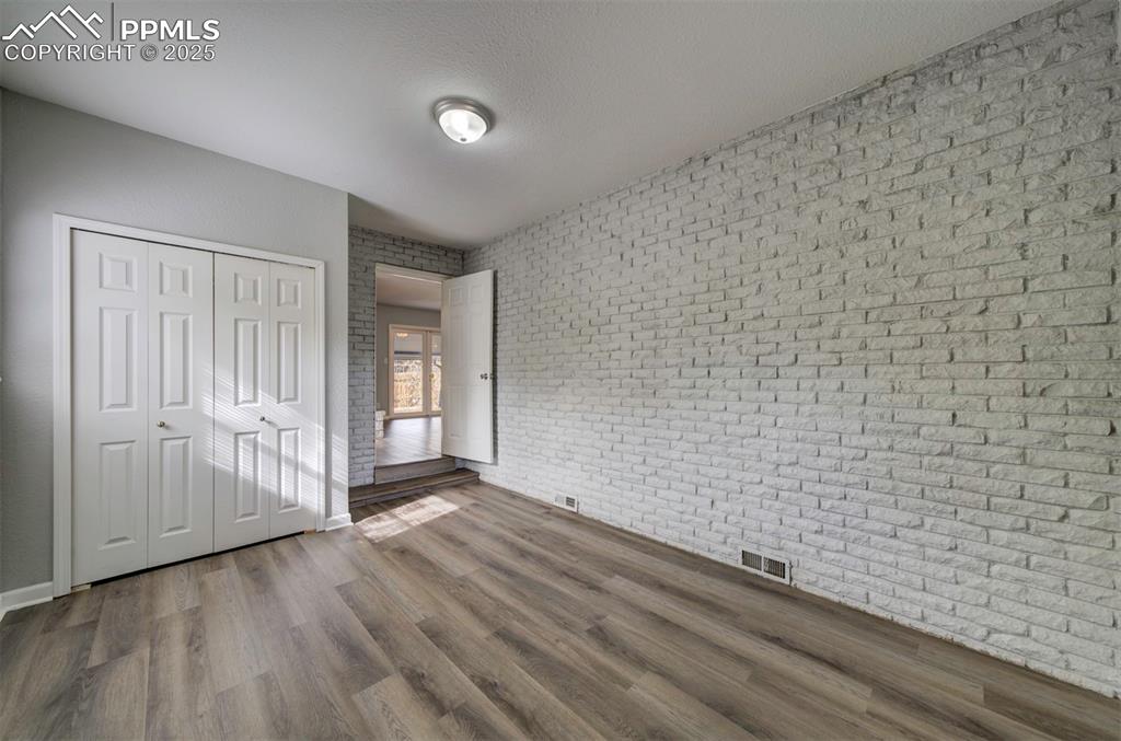 Image 19 of 43: Unfurnished bedroom featuring wood style floors, brick wall, and a closet