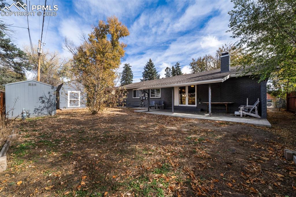 Image 36 of 43: Back of house with 2 sheds, a covered patio area, brick siding, and a chimn