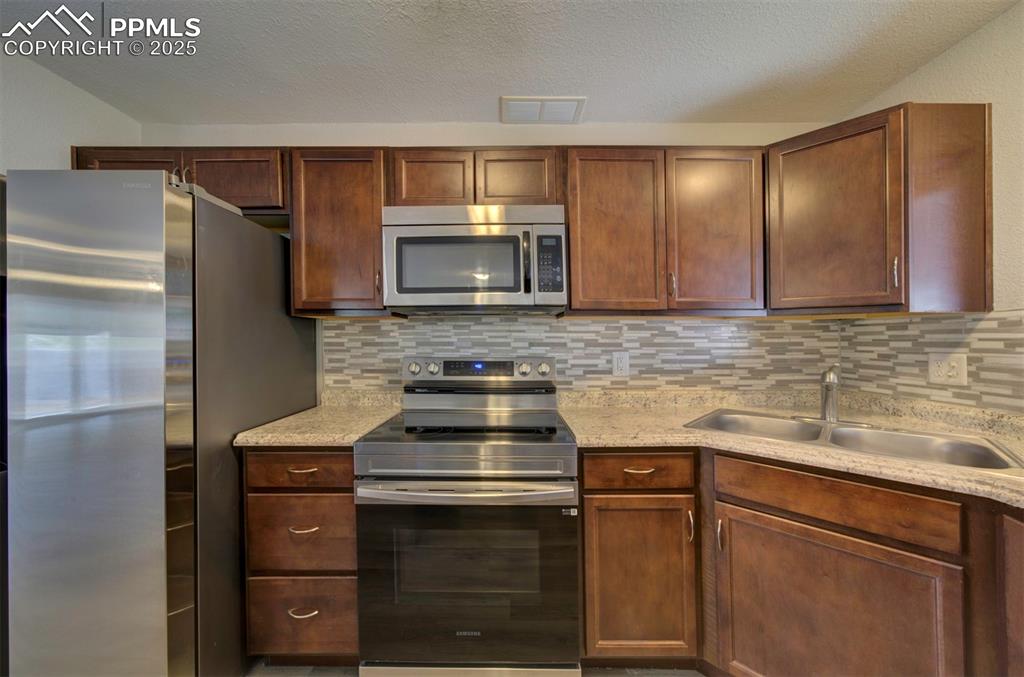 Image 8 of 43: Kitchen with stainless steel appliances, tasteful backsplash, light stone c