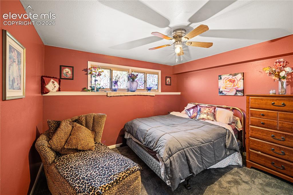 Image 24 of 50: Carpeted room featuring a ceiling fan, a window with curtains, and a crysta