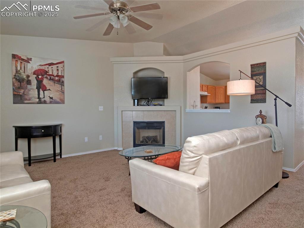 Image 4 of 24: Living room featuring a tiled fireplace, light colored carpet, a ceiling fa