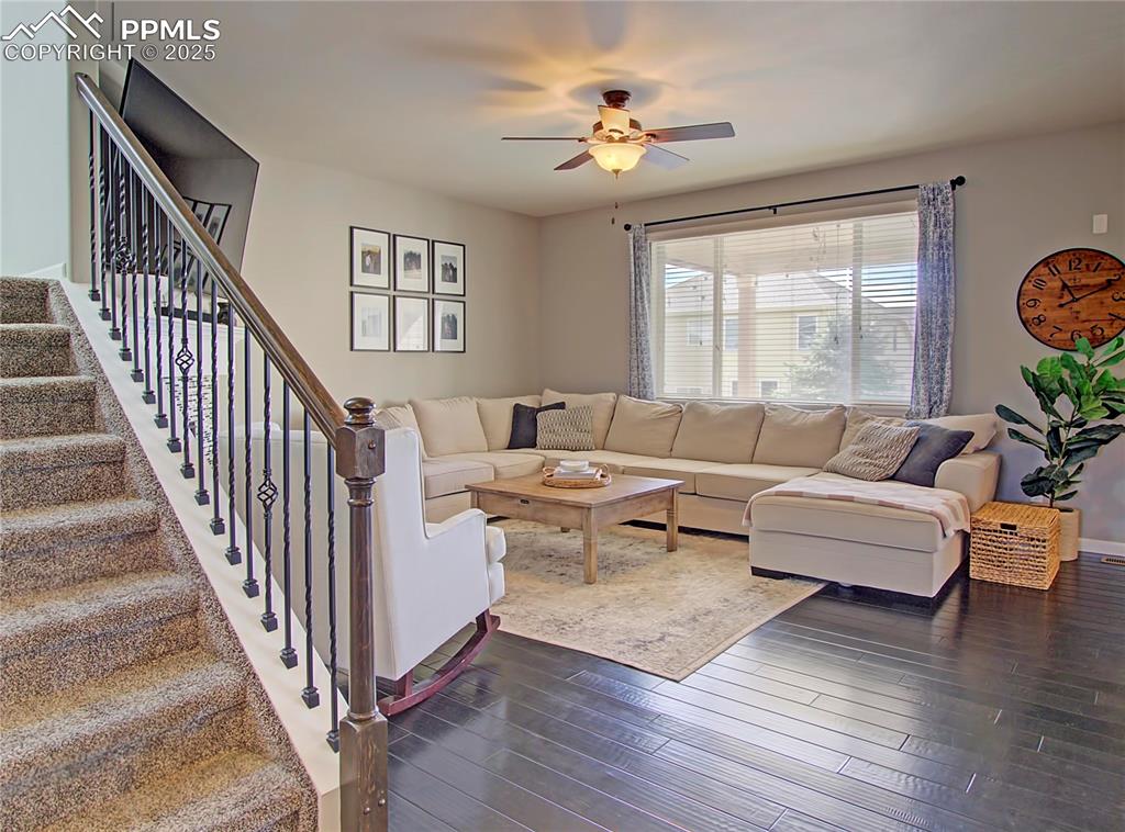 Image 10 of 44: Living area with dark wood finished floors, a ceiling fan, and stairs