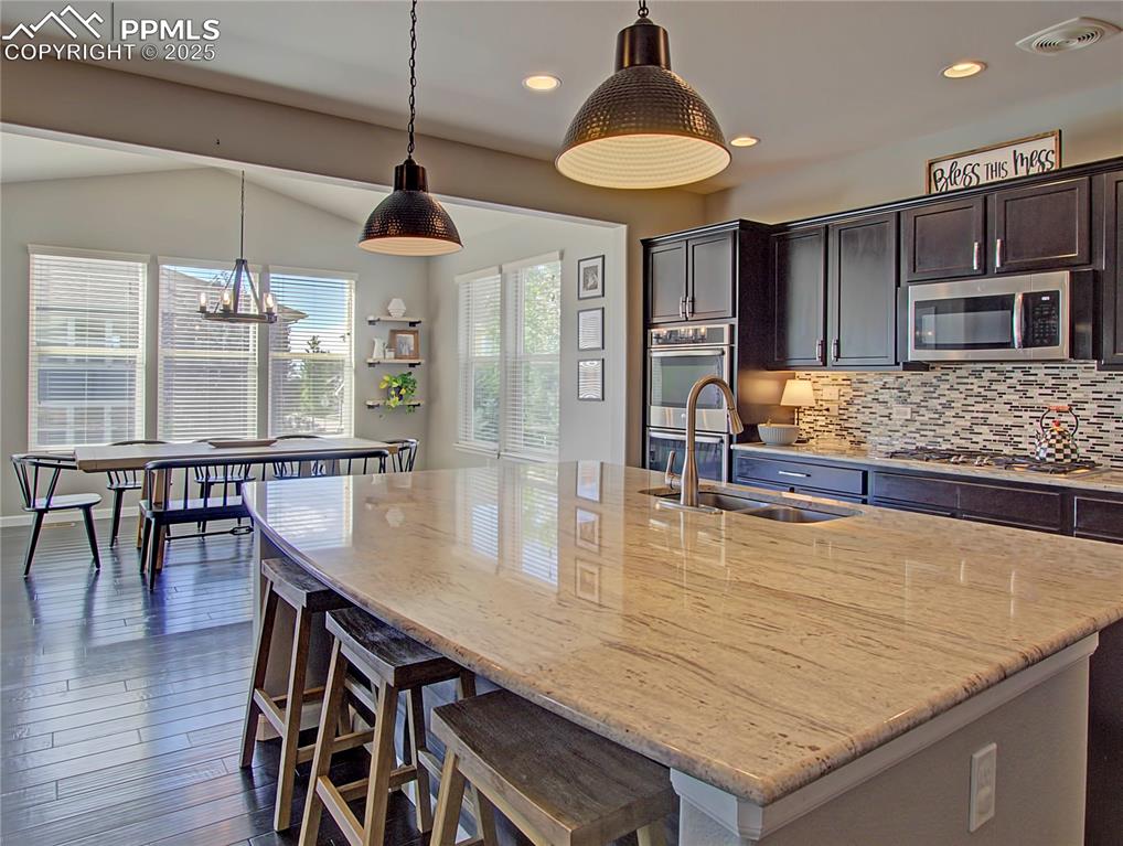 Image 14 of 44: Kitchen featuring a kitchen island with sink, decorative light fixtures, li
