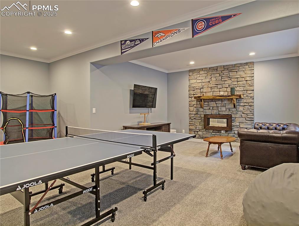 Image 30 of 44: Recreation room with crown molding, a fireplace, light carpet, and recessed