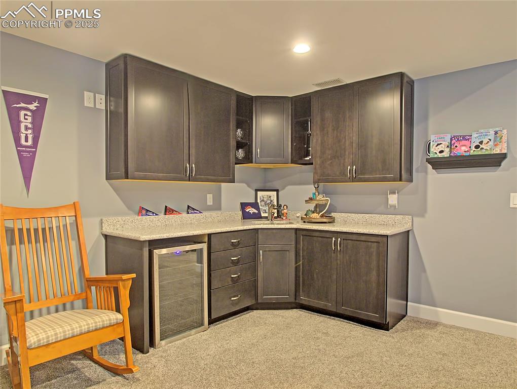 Image 31 of 44: Bar area featuring dark brown cabinets, light colored carpet, wine cooler,