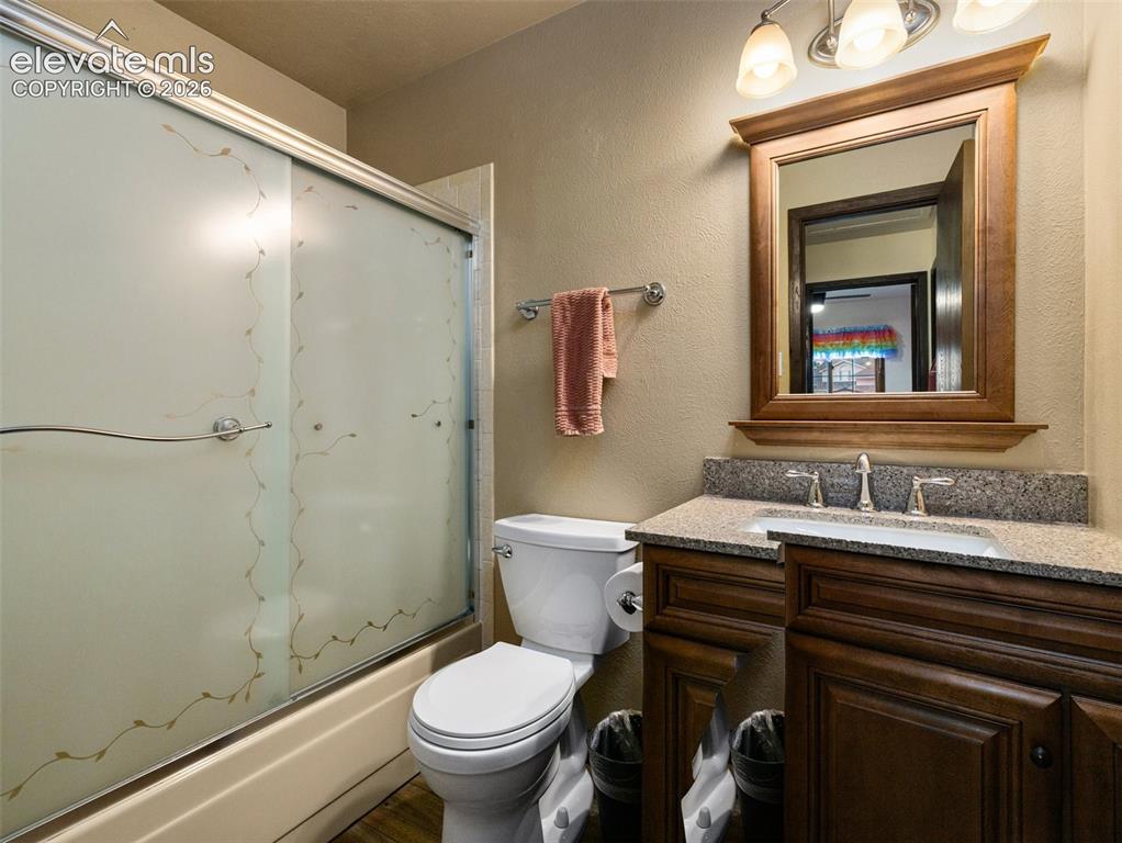 Image 18 of 34: Bathroom featuring a wood-finish vanity with a stone countertop, an undermo