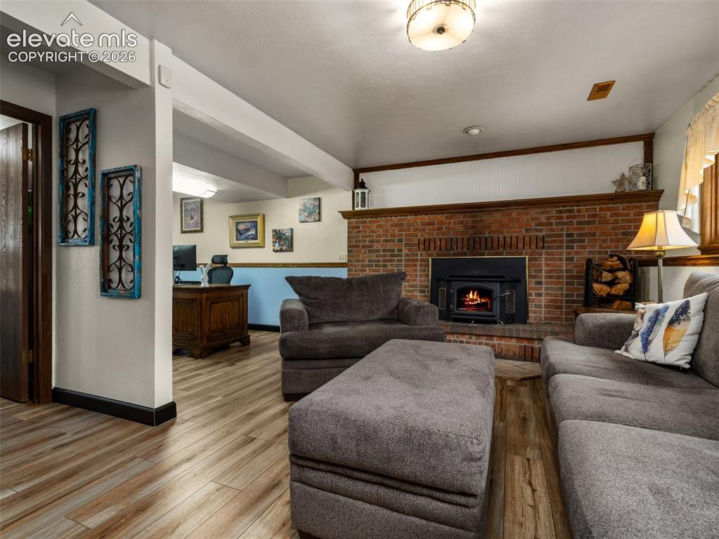 Image 20 of 34: Brick fireplace with a wood-burning insert, wood-finish flooring, and expos