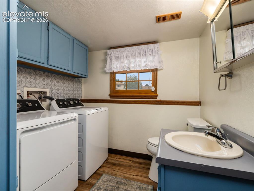 Image 23 of 34: Laundry area featuring wood-finish flooring, patterned tile backsplash, and
