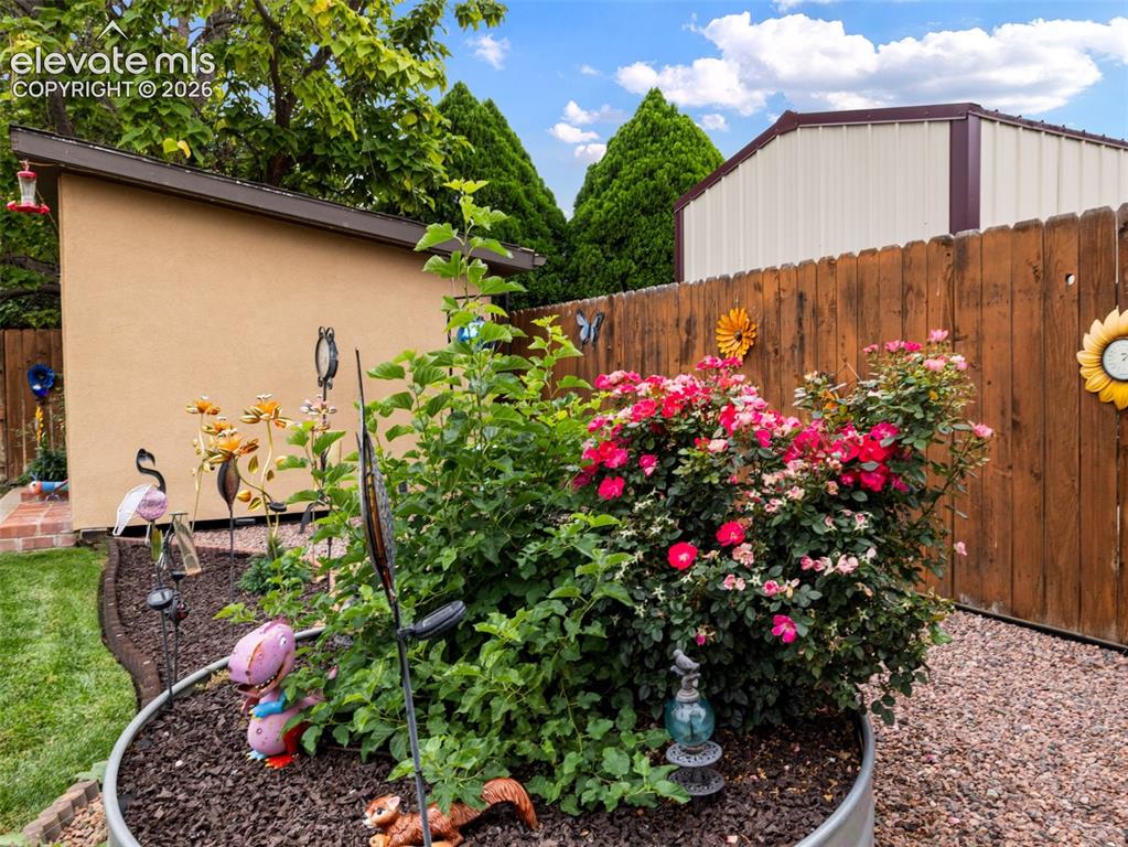 Image 28 of 34: Stucco exterior structure, wood privacy fencing, mature green foliage, vibr