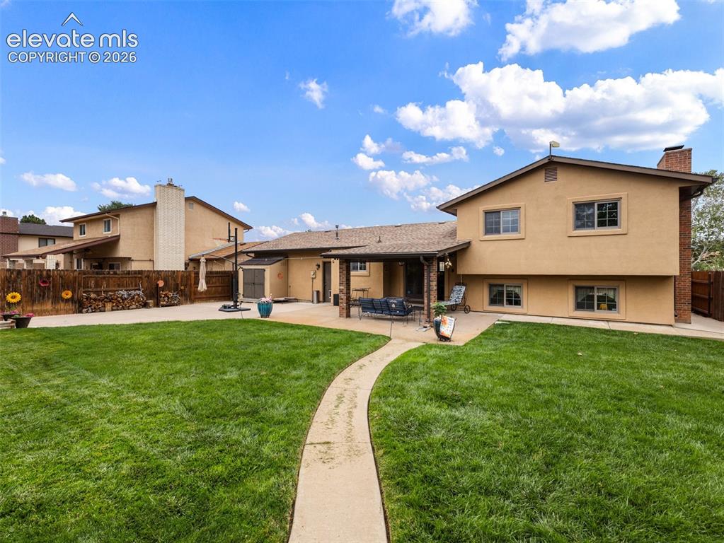 Image 29 of 34: Expansive green lawn with a curved concrete pathway and a stucco exterior h