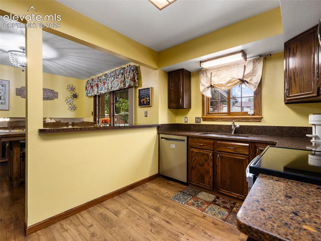 Image 9 of 34: Wood-finish flooring, dark wood cabinetry, and a built-in dishwasher