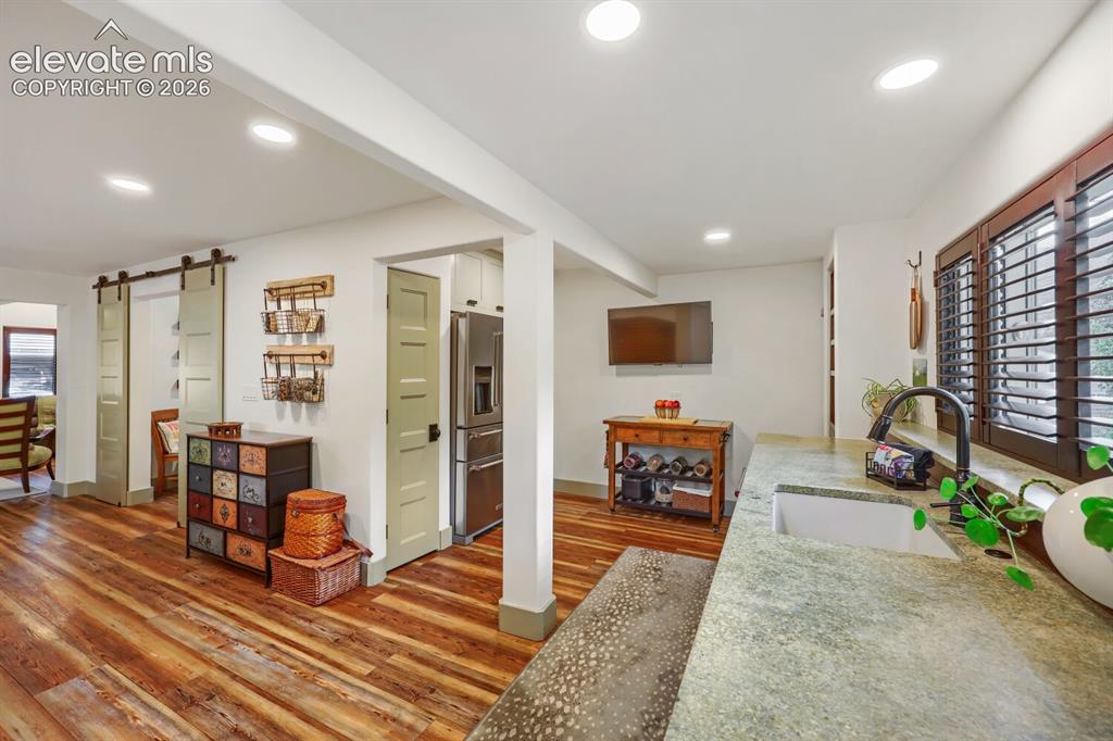 Image 14 of 30: Wood-finish flooring, recessed lighting, and a stainless steel refrigerator