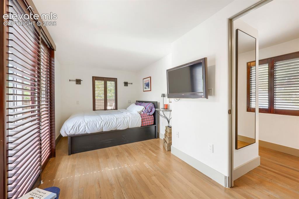 Image 21 of 30: Hardwood flooring, wall-mounted sconce lighting, and wood-toned louvered wi