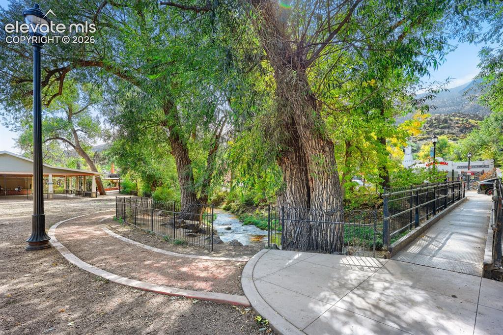 Image 28 of 30: Paved pedestrian paths, a black metal bridge with railings, a flowing creek