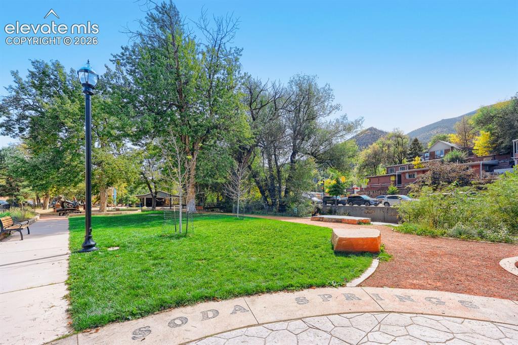 Image 30 of 30: Manicured lawn area with mature trees, stone-look paver path, and a mountai