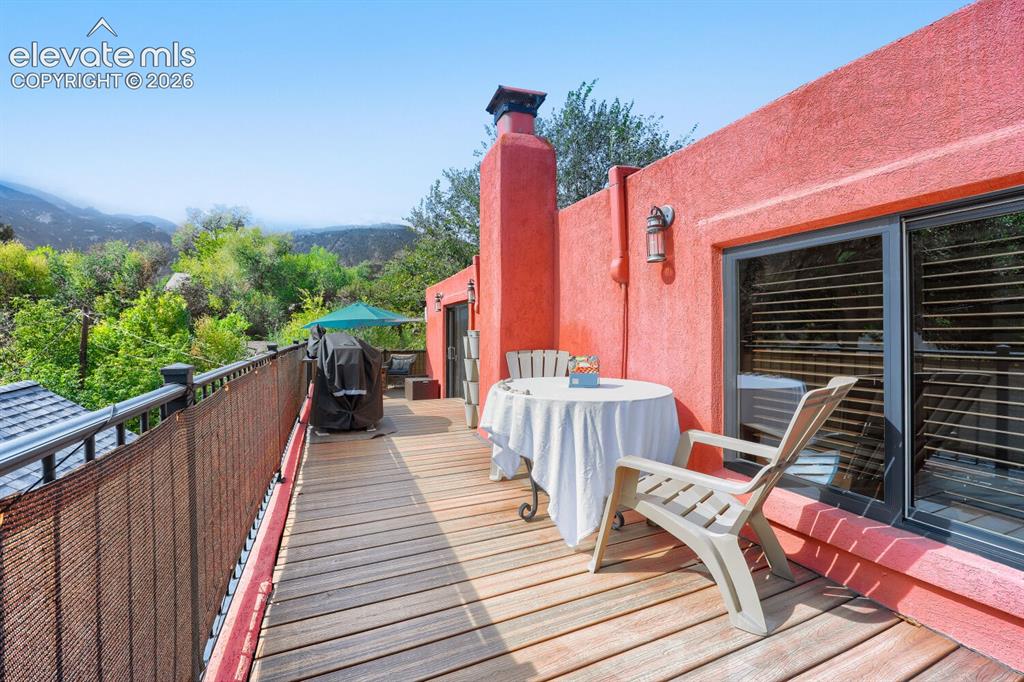 Image 4 of 30: Spacious outdoor deck with wood-finish planks, vibrant red stucco exterior,