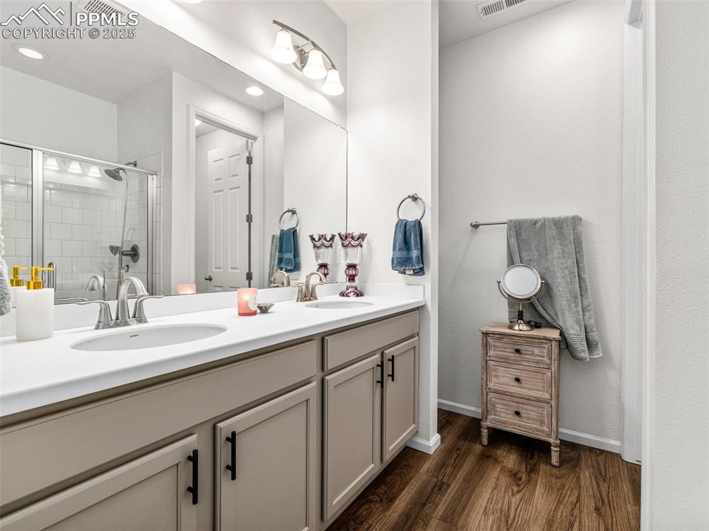 Image 21 of 26: Full bathroom with double vanity, dark wood-type flooring, and a tile showe
