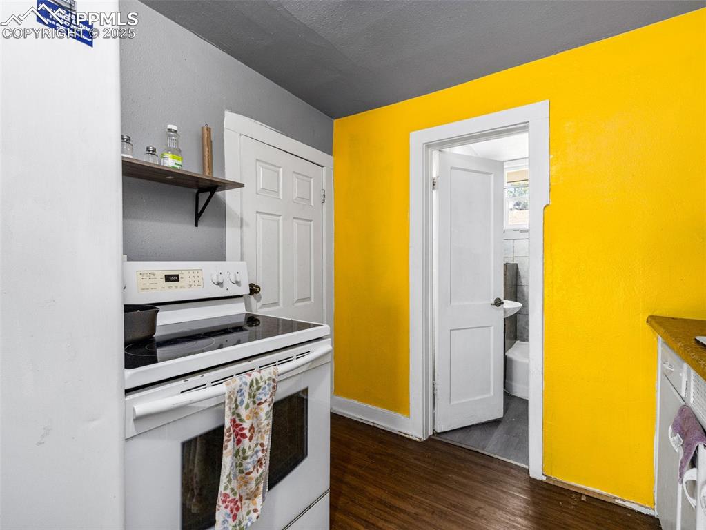 Image 12 of 30: Kitchen with white electric stove, dark wood-style flooring, open shelves,
