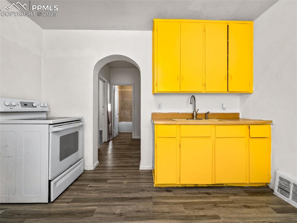 Image 22 of 30: Kitchen with white electric range, arched walkways, dark wood finished floo