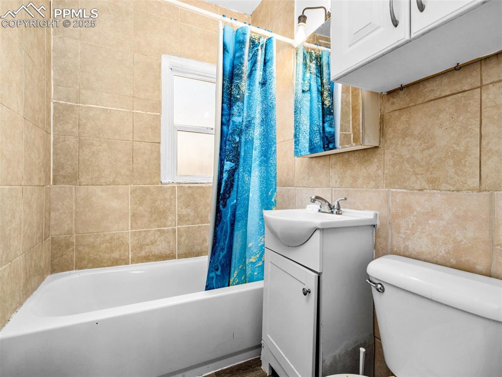 Image 28 of 30: Bathroom featuring shower / bath combination with curtain, tile walls, and
