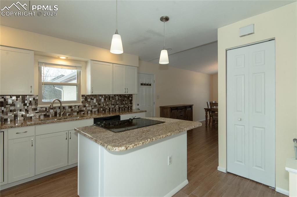 Image 8 of 23: Kitchen with white cabinetry, pendant lighting, light stone countertops, ba