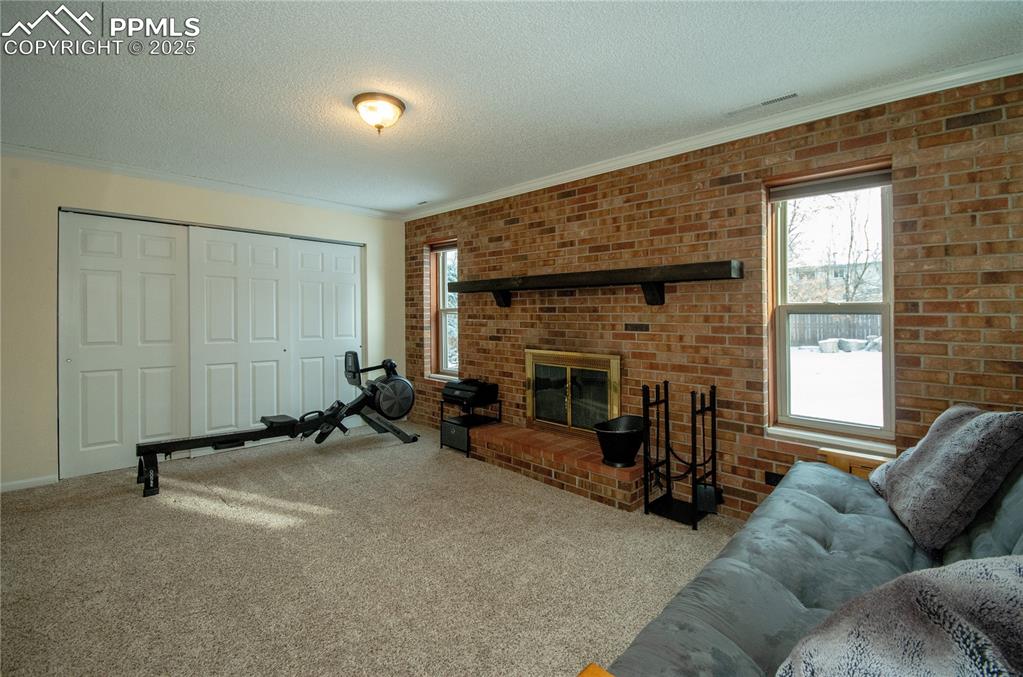 Image 9 of 23: Carpeted living room with a textured ceiling, a brick fireplace, brick wall