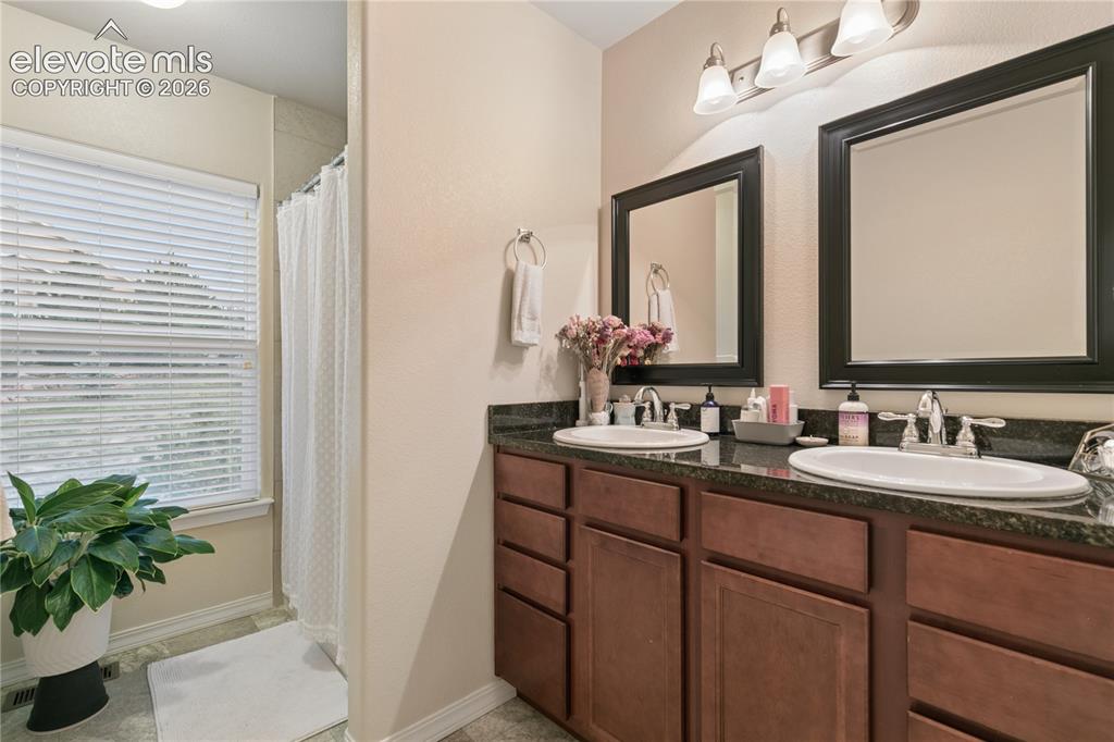 Image 11 of 28: Bathroom featuring a dual vanity with a dark countertop, undermount sinks,