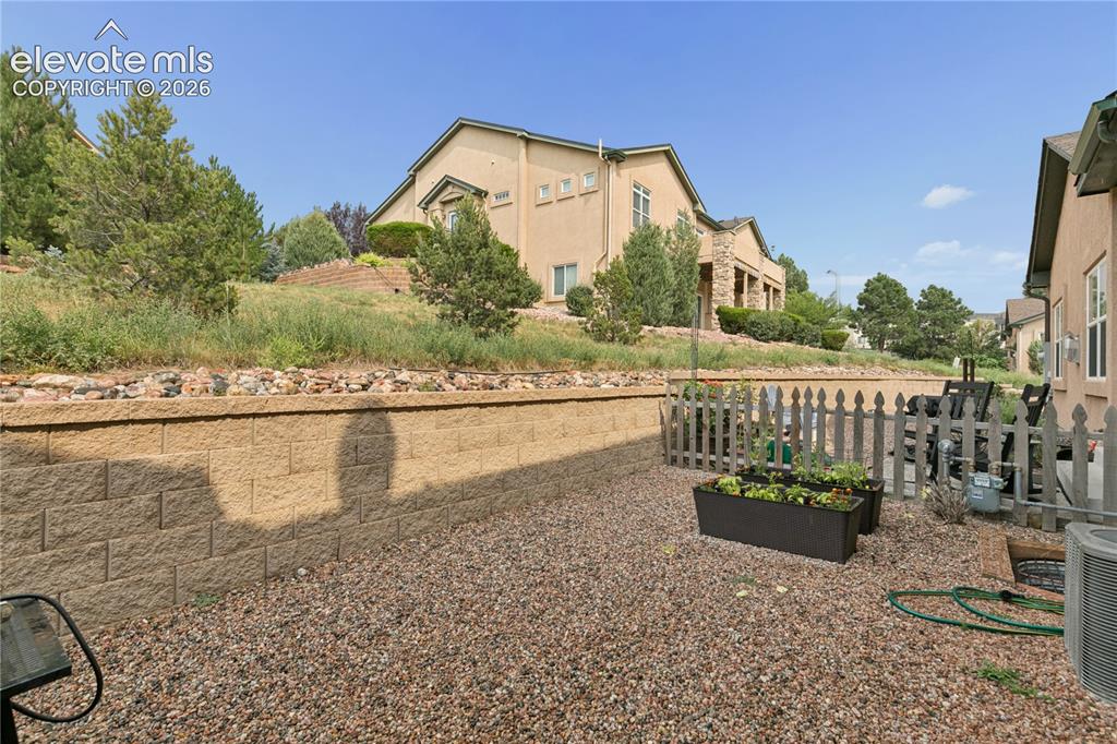 Image 19 of 28: Xeriscaped rear yard featuring a block retaining wall, gravel ground cover,